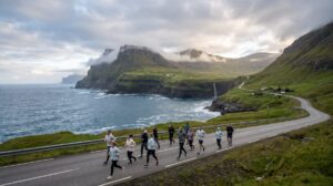 Runners on a coastal road in the Faroe Islands with green cliffs and the North Atlantic behind them during a half marathon.